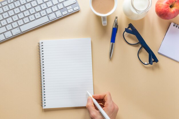 Крупный план руки человека, пишущего на спиральном блокноте с ручкой на бежевом офисном столе