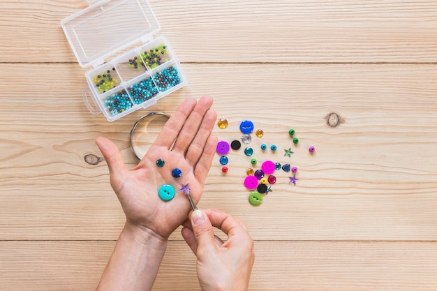 Close-up of a person's holding beads and button with tweezers