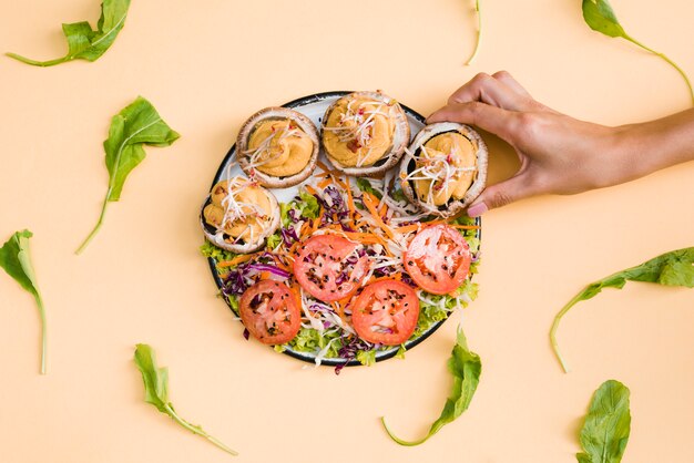 Close-up of a person taking mushroom caps stuffed with creams on plate over the beige backdrop