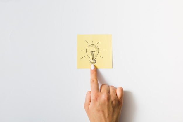 Free photo close-up of a person touching finger on drawn light bulb over the sticky note