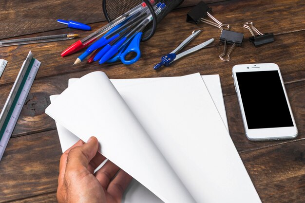 Close-up of a person turning page with stationeries and mobile on table