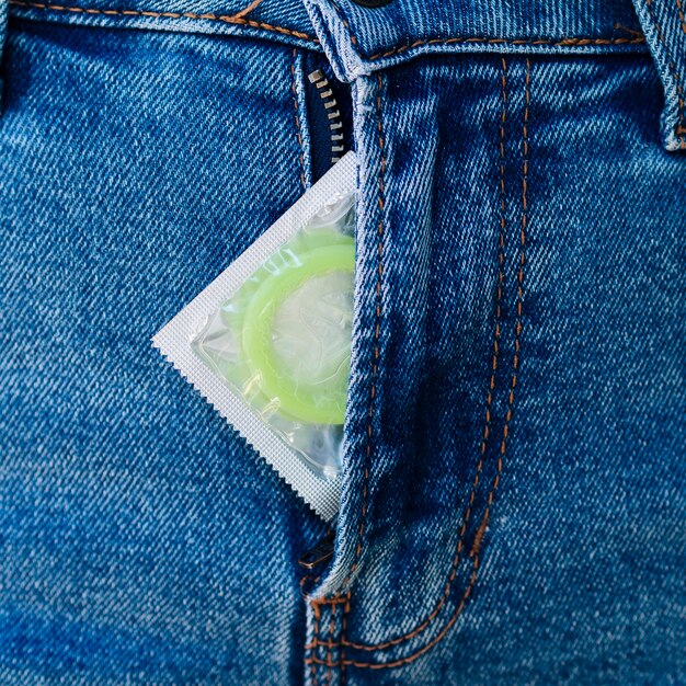 Close-up person with condom in jeans zip