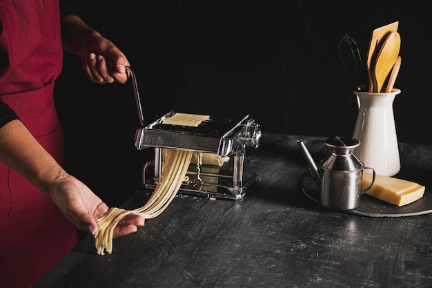 Close-up person with pasta machine and kitchen utensils 