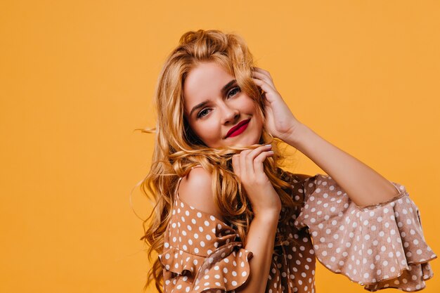 Close-up photo of adorable woman in vintage brown dress. Appealing curly girl in trendy blouse posing on yellow wall.