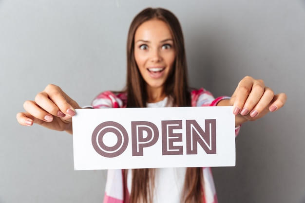 Close-up photo of amazed young brunette woman holding open sign