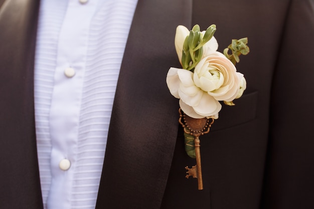 Close up photo of beautiful boutonniere decorated with key on the groom's black jacket.