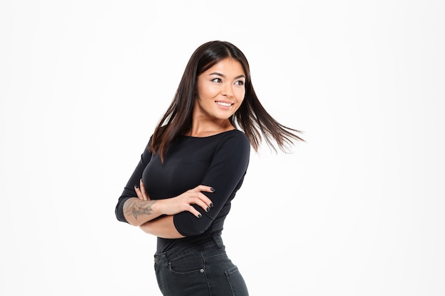 Close-up photo of cheerful asian girl with flying hair standing with crossed hands, looking aside