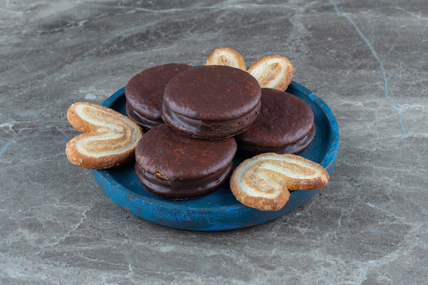 Close up photo of chocolate wafers with homemade cookies on blue wooden plate.