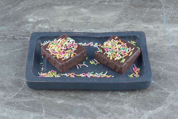 Close up photo of chocolate wafers with sprinkle on grey wooden plate.