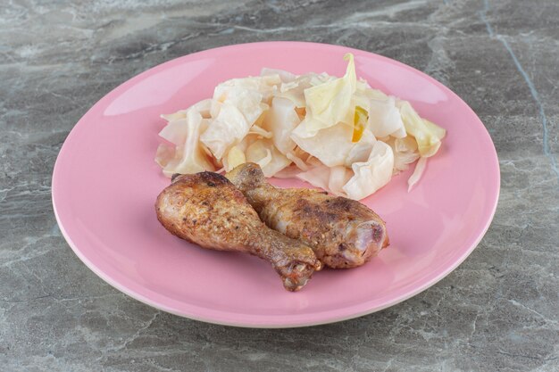 Крупным планом фото нарезанный рассол капусты с куриными голеньями на розовой пластине.