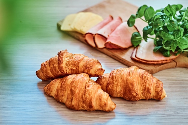 Close-up photo of a croissant with ham and cheese on wooden board.