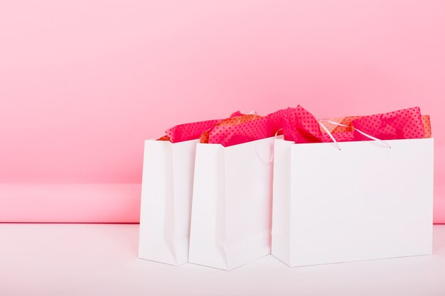 Крупным планом фото милые подарочные пакеты с упаковочной бумагой, лежащей на полу на розовом фоне. Кто-то оставил свои покупки в белых пакетах на подарок на день рождения после совершения покупок в номере.