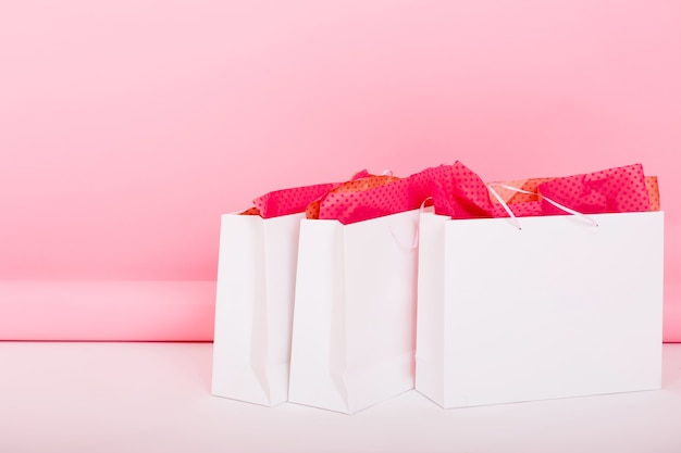 ピンクの背景の床に横たわっている包装紙でかわいいギフトバッグのクローズアップ写真。誰かが部屋で買い物をした後、誕生日プレゼントのために購入品を白いパッケージに入れたままにしました。