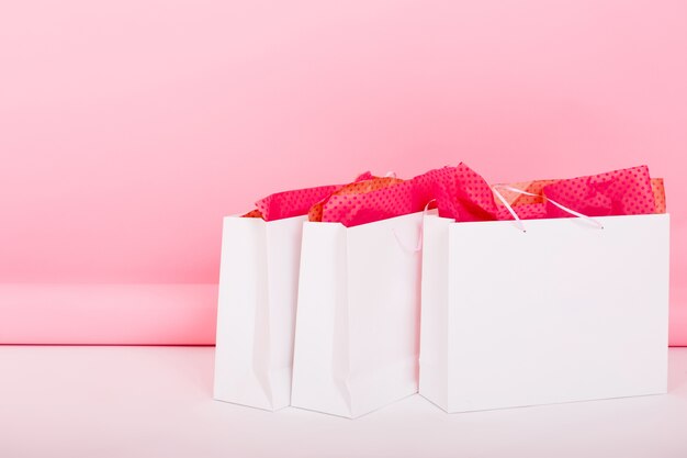 Close-up photo of cute gift bags with wrapping paper lying on the floor on pink background. Someone left their purchases in white packages for a birthday present after shopping in the room.