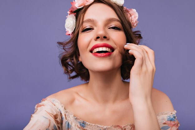 笑っている熱狂的な若い女性のクローズアップ写真。花の輪の中の気さくな女性モデル。