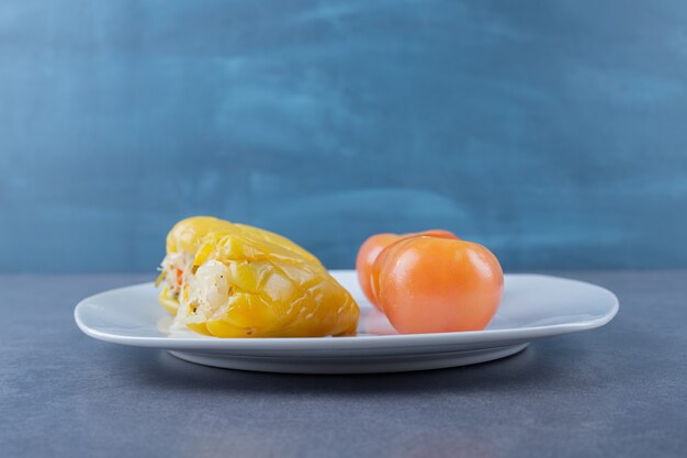 Close up photo of filled green pepper with red tomato on white plate.