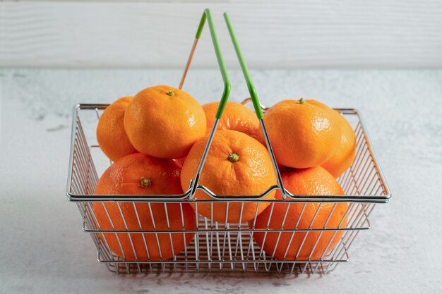 Close up photo of fresh clementine mandarins in basket on grey surface. 