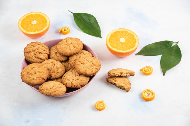 그릇에 담긴 신선한 홈메이드 쿠키와 잎이 있는 땅에 있는 유기농 오렌지를 클로즈업하세요.