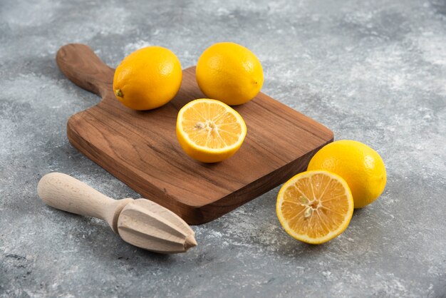 Close up photo of fresh lemons on wooden board with lemon squeezer.