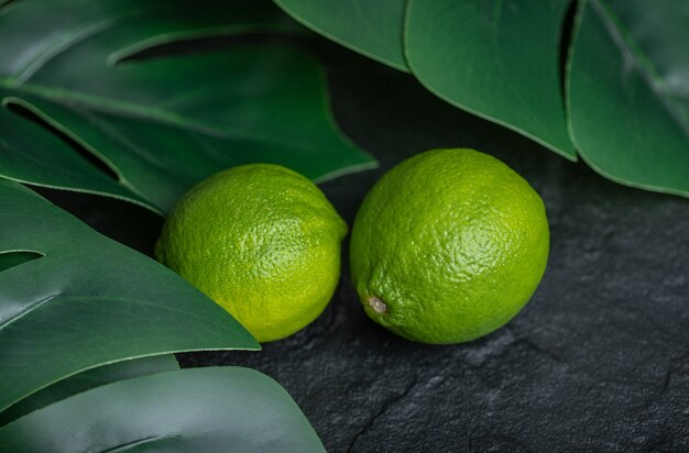 Close up photo of fresh lime with green leaves on black background