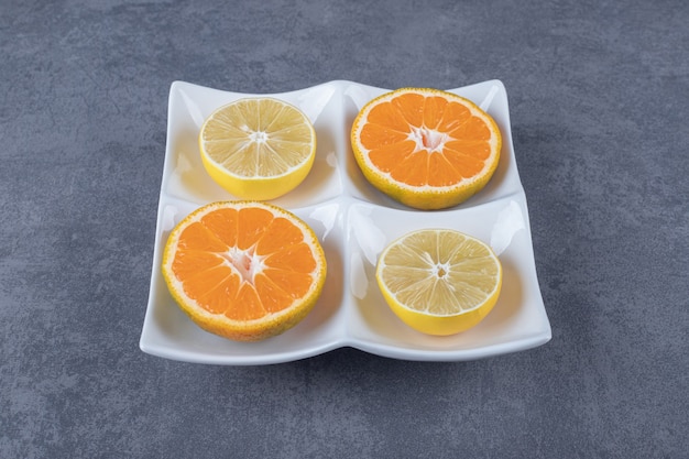 白いプレート上の新鮮なオレンジとレモンのスライスの写真を閉じます。