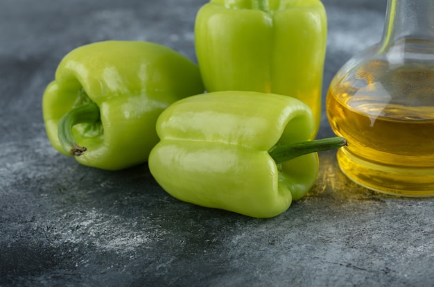 Close up photo of Fresh organic peppers with bottle of oil over grey background. 