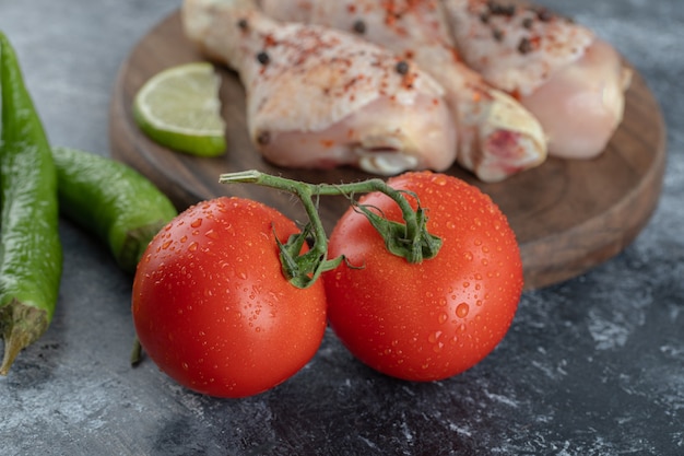 Close up photo of Fresh organic tomatoes and peppers with raw chicken legs .