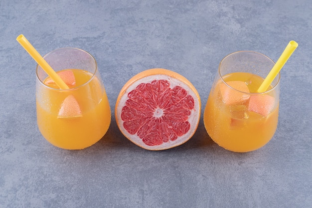 Крупным планом фото свежеприготовленного апельсинового сока со спелым грейпфрутом на сером фоне.