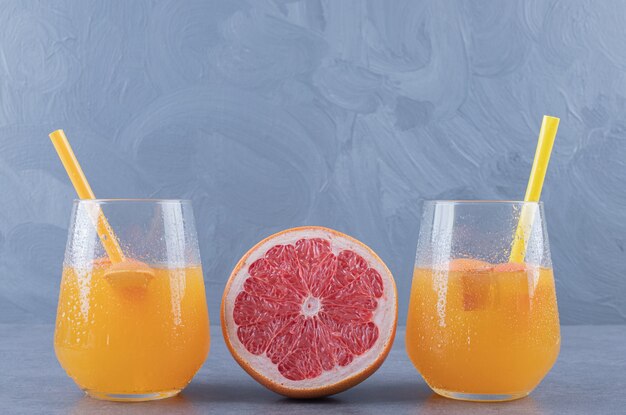 Close up photo of Freshly made orange juice with ripe grapefruit on grey background.