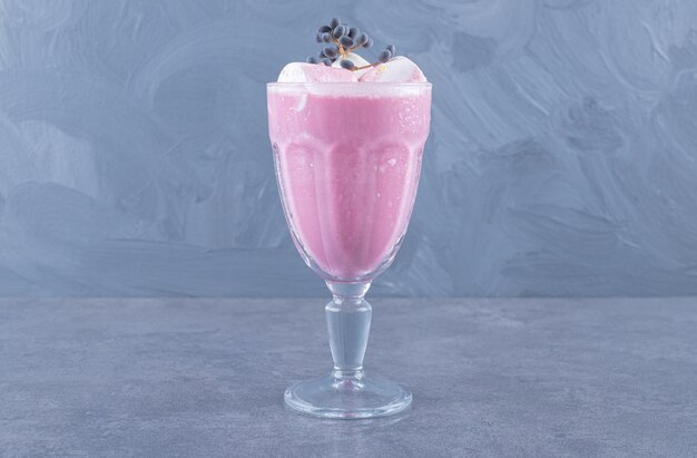 Крупным планом фото свежеприготовленного розового молочного коктейля на сером фоне.
