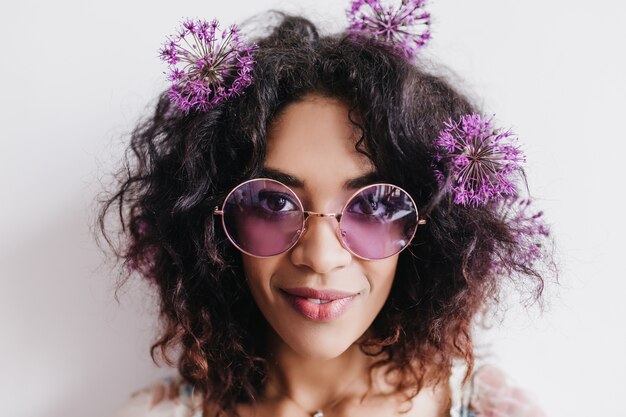 Close-up Photo Of Glad African Woman Posing With Flowers In Hair. Indoor Portrait Of Pleased Black Girl In Sunglasses Isolated.