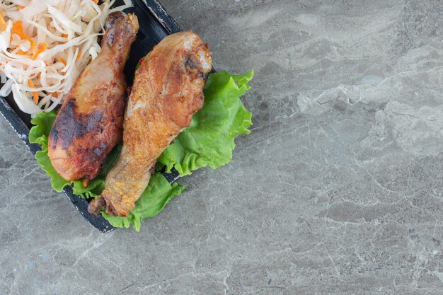 Close up photo of grilled chicken drumsticks with lettuce leaf and sauerkraut. 