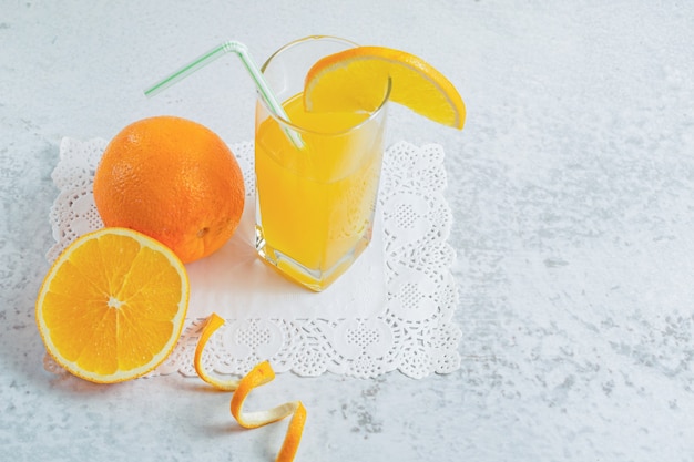 Close up photo of half cut or whole fresh orange with glass of juice on grey wall.