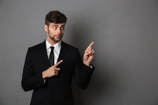 Close-up photo of handsome brunette man in black suit pointing with two fingers upward