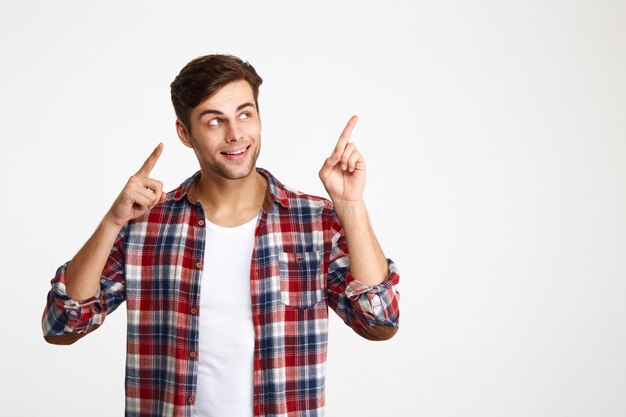Close-up photo of happy attractive young man in checkered shirt pointing with two fingers, looking aside