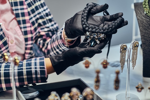 Close-up photo of a jewelry worker presenting a costly necklace with gemstones in a luxury jewelry store.