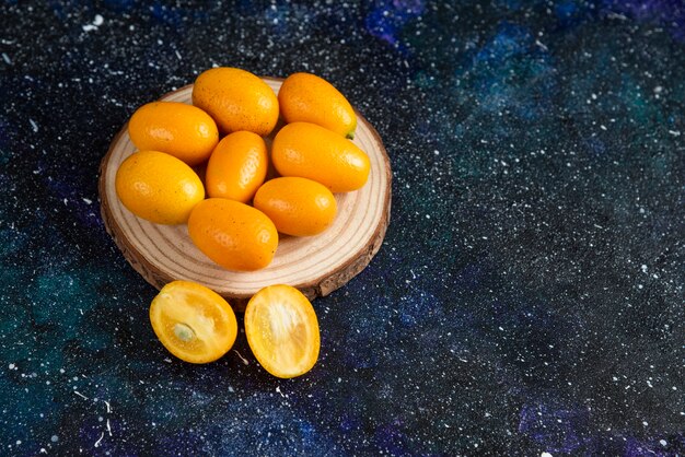 Close up photo of juicy kumquats on wooden board over blue surface