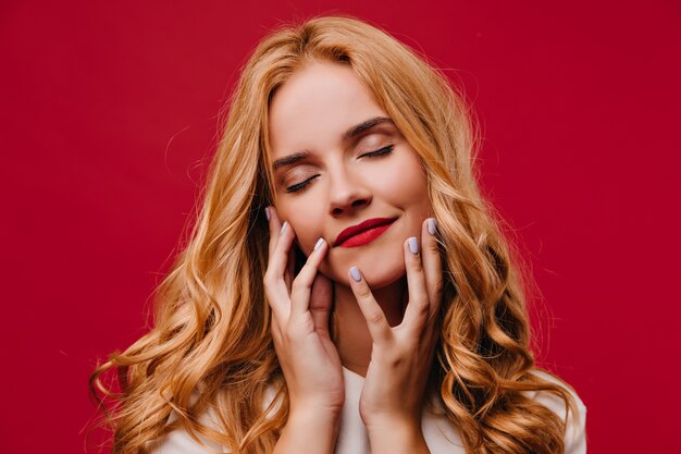 Close-up photo of magnificent white woman. Charming long-haired girl posing on red wall.