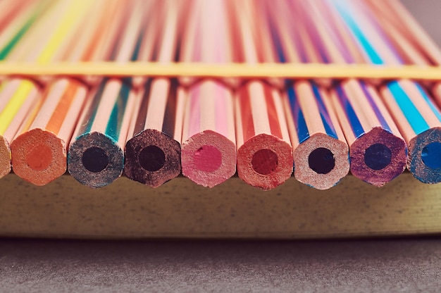 Close-up photo multicolored pencils lying on a yellow notepad.