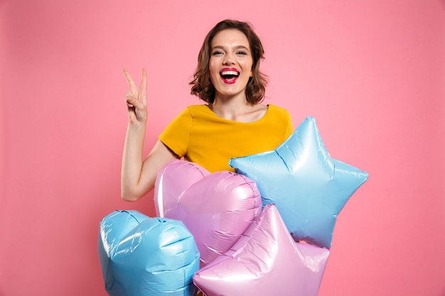 Бесплатное фото Крупным планом фото с днем рождения девушки с красными губами, держа воздушные шары, показывая жест мира,