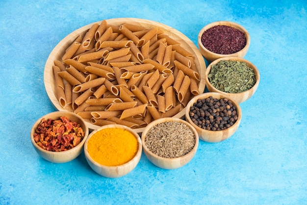 나무 판자에 있는 원시 갈색의 사진과 파란색 탁자 위에 있는 다양한 종류의 향신료를 클로즈업하세요.