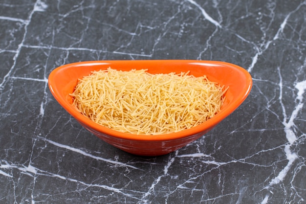 Close up photo of orange bowl full with raw vermicelli.