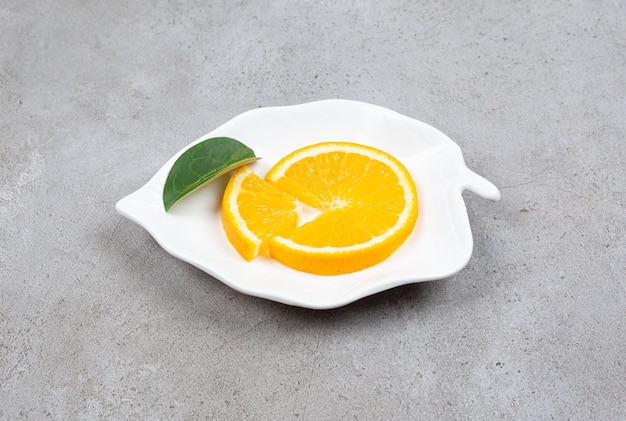 Закройте вверх по фото дольки апельсина с листом на белой тарелке в форме листа.