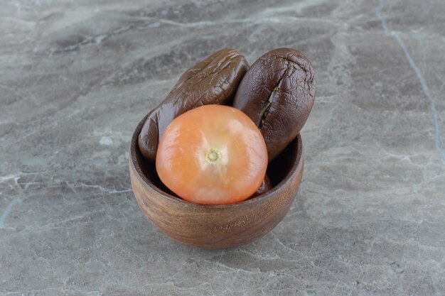 Close up photo of pickled tomato and eggplants in wooden bowl.