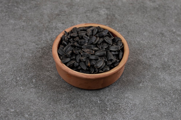 Close up photo. Pile of sunflower seeds in pottery bowl over grey surface. 
