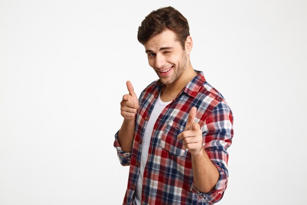 Close-up photo of playful shaven young man in checkered shirt pointing with two fingers