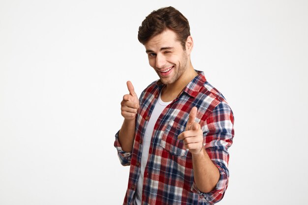 Фото крупного плана игривого выбритого молодого человека в клетчатой рубашке, указывая двумя пальцами