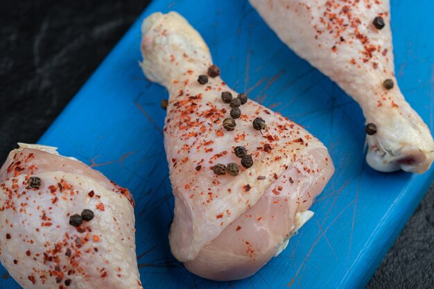 Close up photo of raw spicy chicken drumstick on blue wooden board.