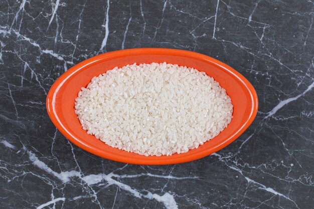 Close up photo of raw uncooked rice in orange bowl.