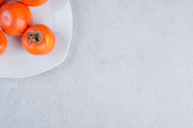 Закройте вверх по фото спелых оранжевых фруктов хурмы. На белой тарелке.
